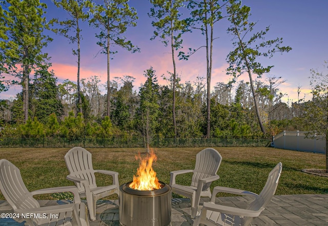 patio terrace at dusk with fence, a fire pit, and a lawn