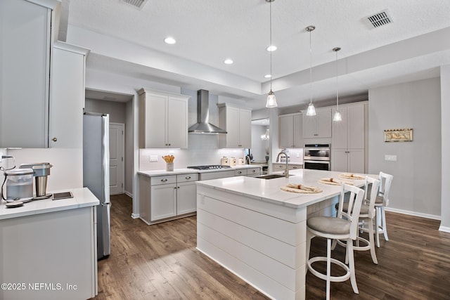 kitchen featuring dark wood-style floors, a center island with sink, visible vents, a sink, and wall chimney exhaust hood