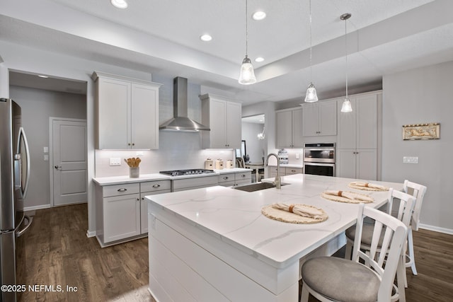 kitchen featuring recessed lighting, dark wood-style flooring, a sink, appliances with stainless steel finishes, and wall chimney exhaust hood