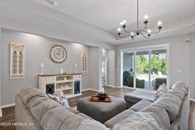 living area with dark wood finished floors, a tray ceiling, a notable chandelier, and baseboards