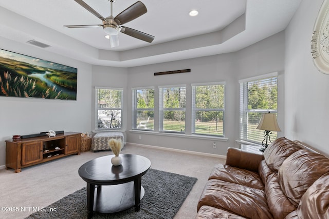 living area with a wealth of natural light, visible vents, baseboards, and a tray ceiling