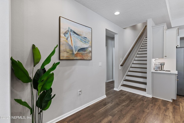 staircase with a textured ceiling, baseboards, and wood finished floors