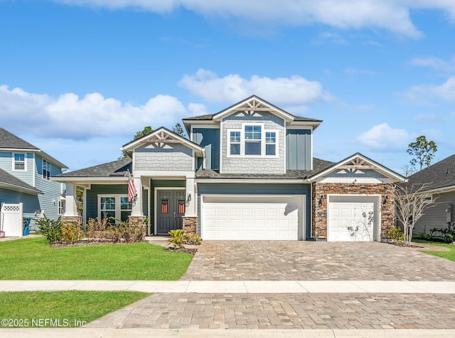 view of front of home with decorative driveway, stone siding, a garage, and a front lawn