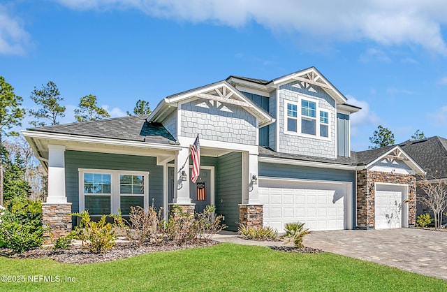 craftsman-style house with a front lawn, decorative driveway, a garage, and stone siding