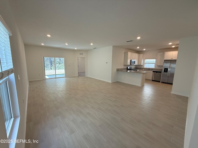 unfurnished living room featuring recessed lighting, baseboards, a sink, and light wood finished floors