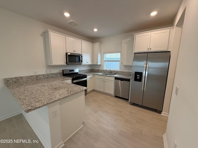 kitchen featuring a sink, light stone counters, appliances with stainless steel finishes, a peninsula, and white cabinets