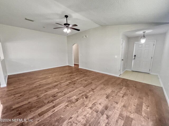 empty room with ceiling fan, vaulted ceiling, a textured ceiling, and light hardwood / wood-style floors