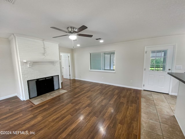 unfurnished living room with brick wall, ceiling fan, light hardwood / wood-style flooring, and a fireplace