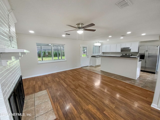 unfurnished living room with light tile floors, ceiling fan, sink, and a fireplace