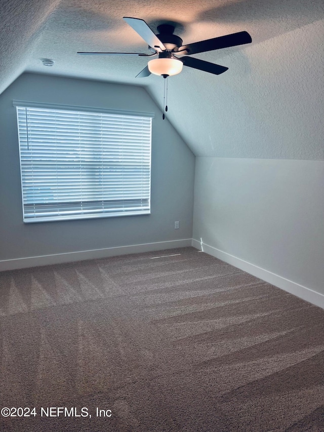 additional living space with a textured ceiling, dark carpet, lofted ceiling, and ceiling fan