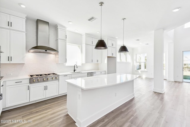 kitchen with stainless steel appliances, a kitchen island, sink, and wall chimney range hood