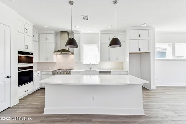 kitchen with white cabinetry, a kitchen island, and wall chimney range hood