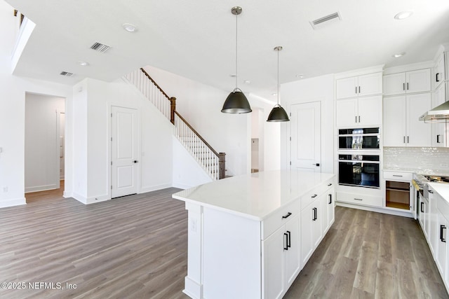 kitchen with a kitchen island, pendant lighting, double oven, white cabinets, and light hardwood / wood-style floors