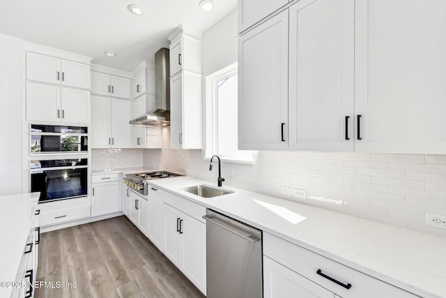 kitchen featuring sink, wall chimney range hood, stainless steel appliances, decorative backsplash, and white cabinets