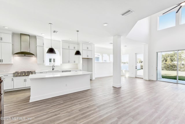 kitchen featuring pendant lighting, wall chimney range hood, white cabinetry, stainless steel gas cooktop, and a kitchen island