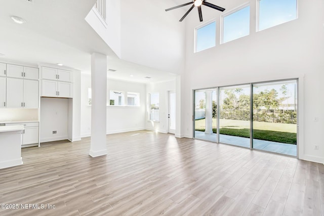 unfurnished living room featuring ceiling fan, decorative columns, a high ceiling, and light wood-type flooring