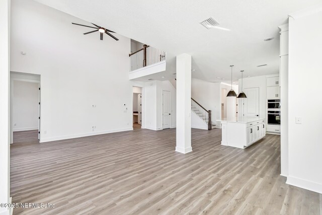 unfurnished living room featuring light hardwood / wood-style floors, ceiling fan, and a high ceiling