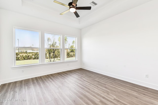 empty room with a raised ceiling, ceiling fan, and light hardwood / wood-style flooring