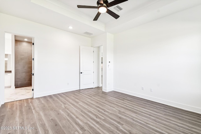 unfurnished bedroom with ceiling fan, ensuite bath, a raised ceiling, and light hardwood / wood-style flooring