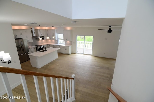 kitchen with a kitchen island with sink, sink, wall chimney exhaust hood, light wood-type flooring, and stainless steel appliances