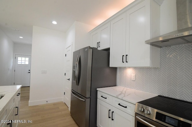 kitchen featuring light stone countertops, appliances with stainless steel finishes, light hardwood / wood-style flooring, and wall chimney range hood