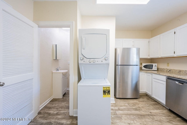 kitchen featuring white cabinetry, stacked washer / drying machine, light hardwood / wood-style flooring, stainless steel appliances, and light stone counters