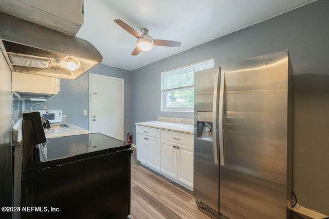 kitchen with ceiling fan, wall chimney range hood, stainless steel refrigerator with ice dispenser, white cabinetry, and light wood-type flooring