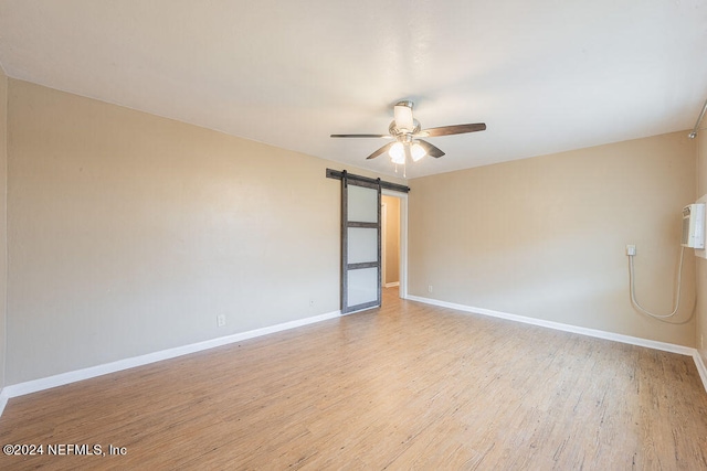 spare room with a barn door, ceiling fan, and light hardwood / wood-style flooring