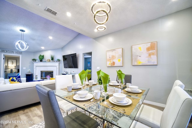 dining area featuring a textured ceiling, light hardwood / wood-style flooring, vaulted ceiling, and a fireplace