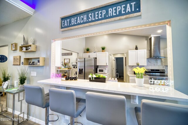 kitchen with white cabinetry, stainless steel fridge with ice dispenser, electric stove, wall chimney range hood, and tasteful backsplash