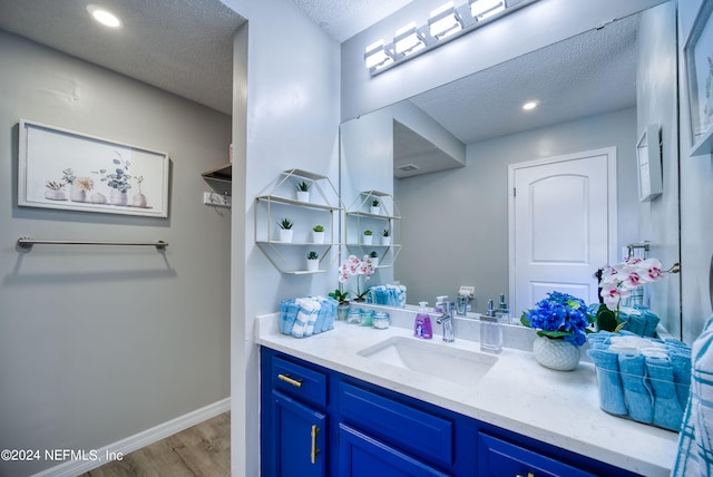 bathroom with a textured ceiling, vanity with extensive cabinet space, and hardwood / wood-style flooring