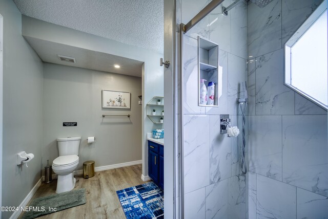 bathroom featuring vanity, hardwood / wood-style floors, a shower with door, a textured ceiling, and toilet