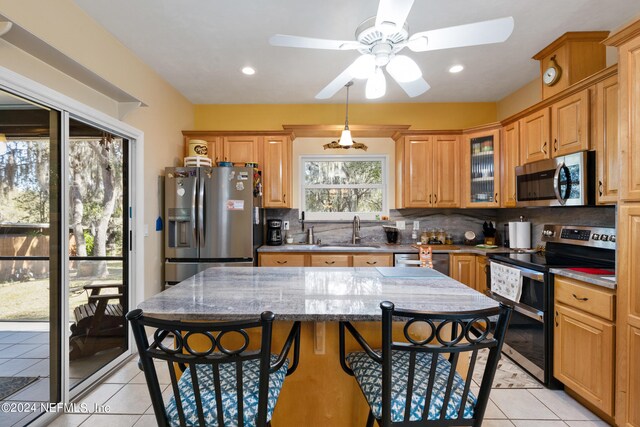 kitchen with ceiling fan, a breakfast bar, appliances with stainless steel finishes, light stone counters, and tasteful backsplash