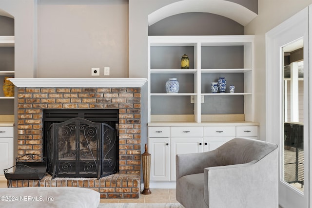 living room featuring built in shelves, a fireplace, and light tile floors