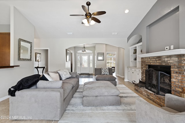 living room featuring lofted ceiling, ceiling fan, built in shelves, and a brick fireplace