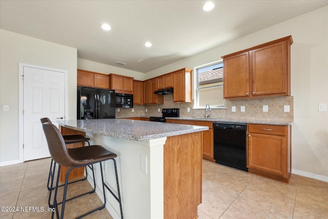 kitchen with backsplash, black appliances, a breakfast bar, and a kitchen island