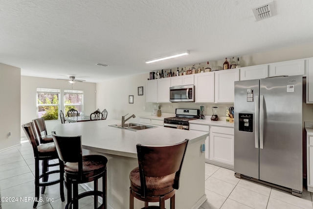 kitchen featuring ceiling fan, white cabinets, a center island with sink, stainless steel appliances, and a kitchen bar