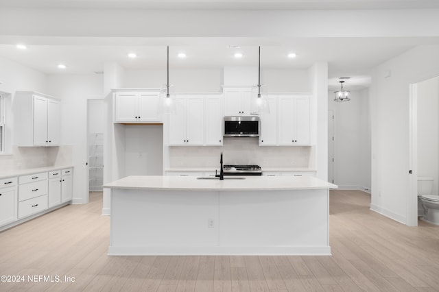 kitchen with stainless steel microwave, a sink, light wood finished floors, and an island with sink