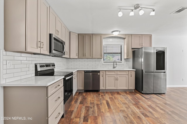 kitchen with appliances with stainless steel finishes, tasteful backsplash, rail lighting, sink, and dark hardwood / wood-style flooring