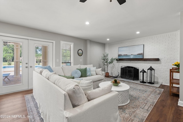 living room featuring a fireplace, french doors, dark wood-type flooring, brick wall, and ceiling fan