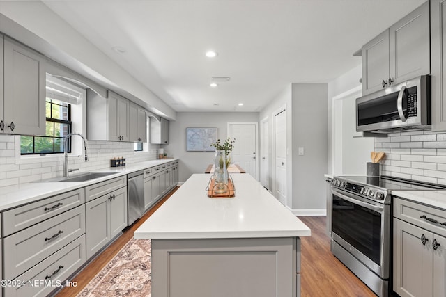 kitchen with a center island, gray cabinetry, light hardwood / wood-style flooring, stainless steel appliances, and sink