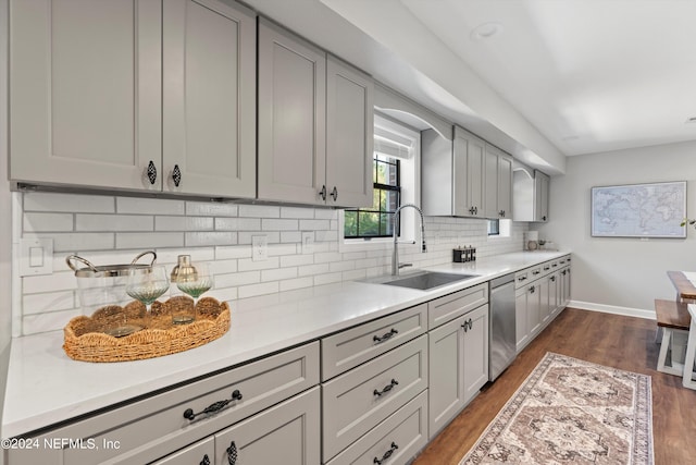 kitchen with sink, tasteful backsplash, gray cabinetry, dark wood-type flooring, and stainless steel dishwasher