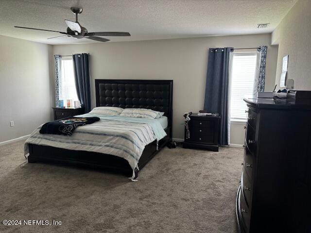 carpeted bedroom featuring ceiling fan and a textured ceiling