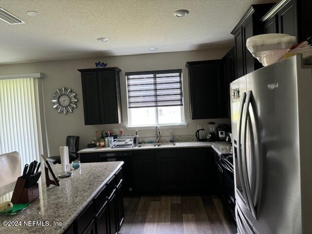 kitchen with a textured ceiling, dark wood-type flooring, black range with electric stovetop, sink, and stainless steel refrigerator