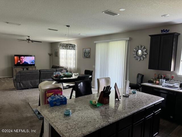 kitchen with dark colored carpet, decorative light fixtures, a textured ceiling, and a kitchen island