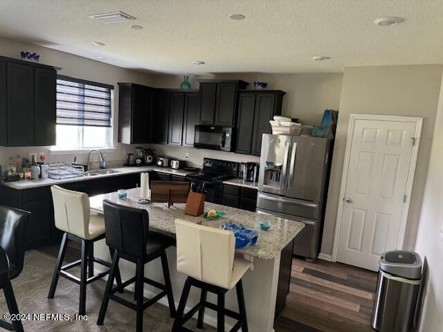 kitchen featuring a kitchen island, black appliances, light stone counters, a breakfast bar, and sink