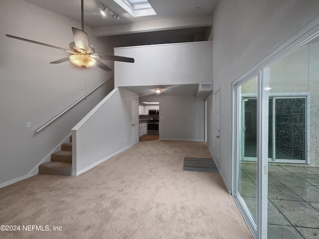 interior space with a skylight, ceiling fan, track lighting, light carpet, and a towering ceiling