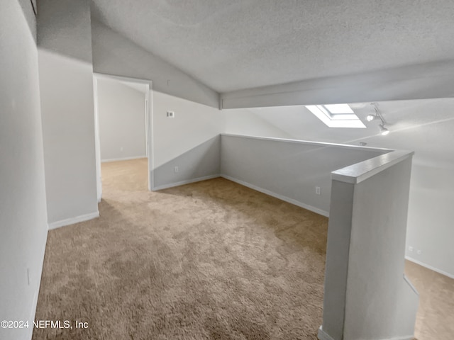 additional living space featuring light carpet, vaulted ceiling with skylight, and a textured ceiling