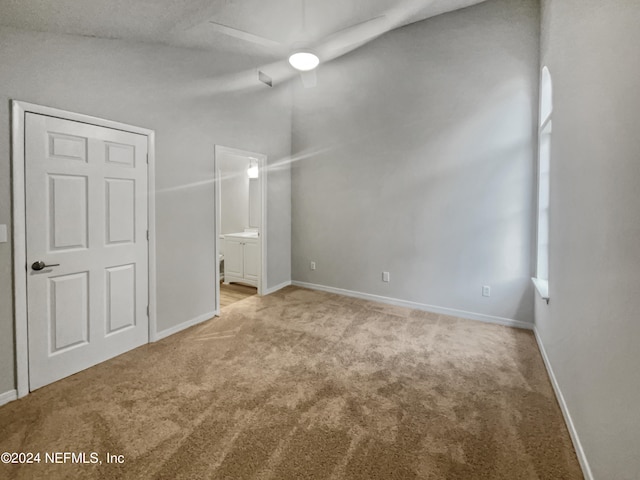 unfurnished bedroom with light carpet, connected bathroom, vaulted ceiling, and ceiling fan