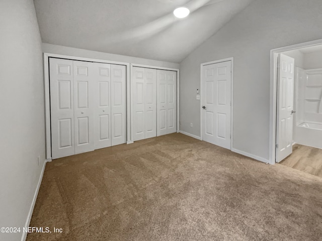 unfurnished bedroom with ensuite bath, two closets, vaulted ceiling, and light colored carpet